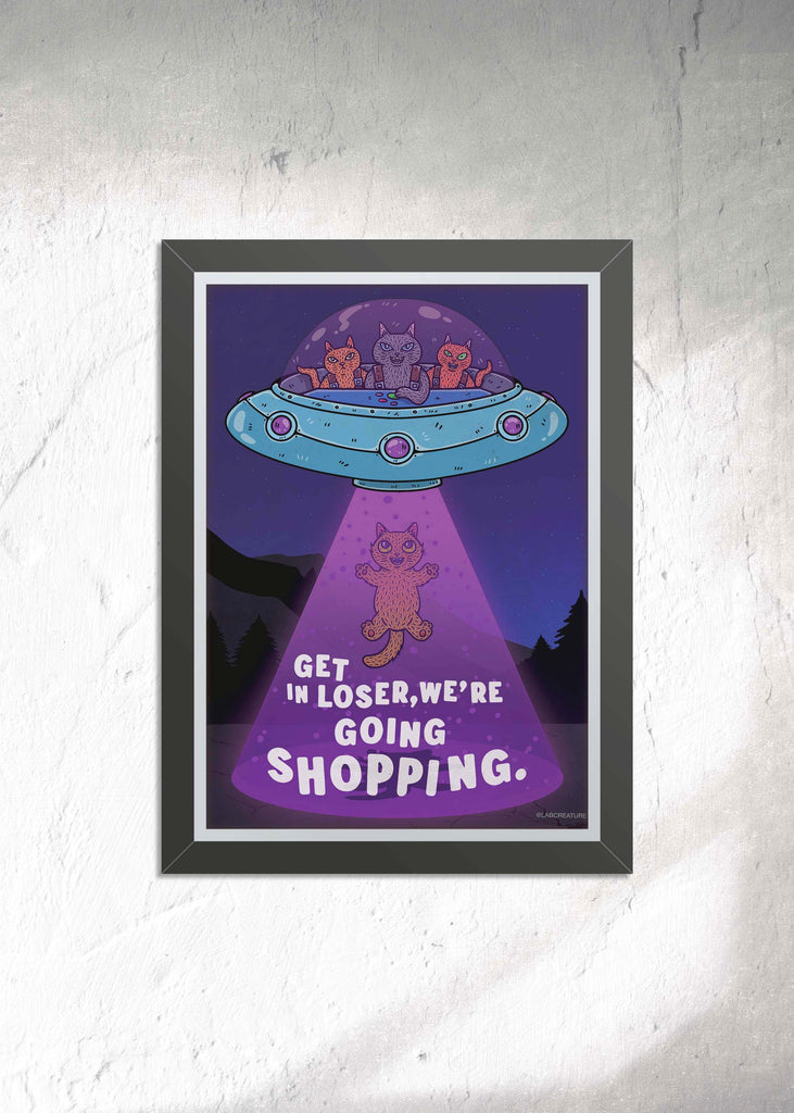 Full color illustration of a framed art print featuring a blue sky with a UFO filled with three cat pilots with a tractor beam abducting an orange cat with mountains in the background